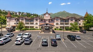 A multi-story hotel with a central entrance, parking lot, and mountainous backdrop. - Swiss Mountain Escape | Pool | Hot Tub | Tennis (Midway)