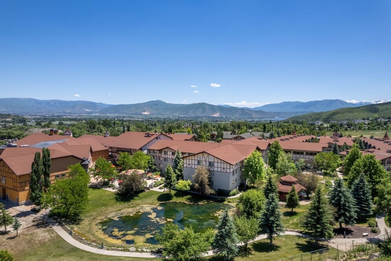 A residential area with multiple buildings, a small pond, and a mountainous backdrop.
