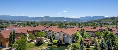 A residential area with multiple buildings, a small pond, and a mountainous backdrop.
