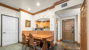 A dining area with a wooden table and chairs, a kitchen in the background, and a door to the right. - Swiss Mountain Escape | Pool | Hot Tub | Tennis (Midway)