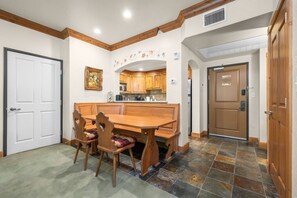 A dining area with a wooden table and chairs, a kitchen in the background, and a door to the right. - Swiss Mountain Escape | Pool | Hot Tub | Tennis (Midway)