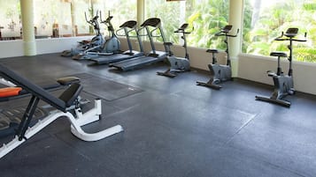 A gym with stationary bikes and a bench, large windows with a view of greenery.