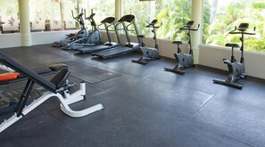 Un gimnasio con bicicletas estáticas y un banco, ventanas amplias con vista a zonas verdes.