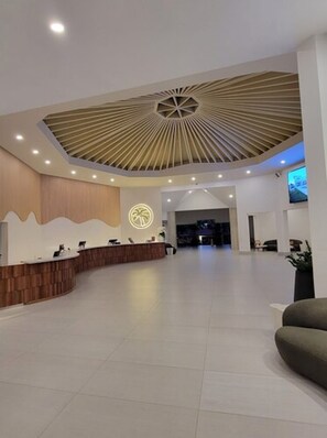 Un moderno vestíbulo de hotel con una recepción, un ventilador de techo grande y una pantalla de televisión.