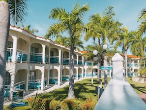 A hotel with multiple balconies, palm trees, and a gift shop sign. - VIP COFRESI BEACH STUDIO ROOM ONLY (Puerto Plata)
