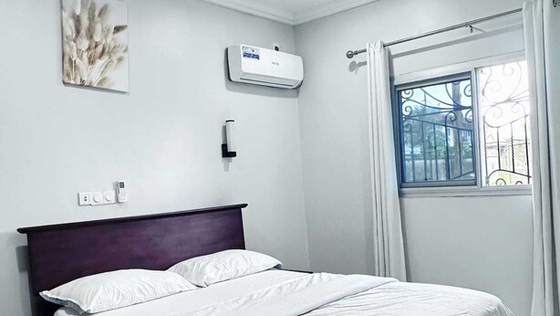 Ein ordentlich bezogenes Bett in einem Zimmer mit Fenster, Wandklimaanlage und Steckdose.