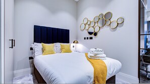 A hotel room with a bed, a headboard, a wall-mounted mirror, and a stack of towels. - Hybrid Resi Canary Wharf One bedroom Apartment (London)