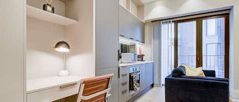 A modern kitchen with a dining area, a sofa, and a view of the city through large windows.