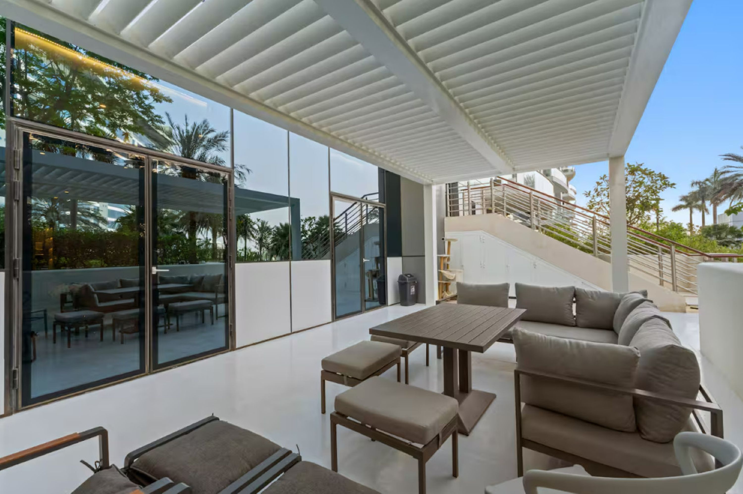 Un espacio exterior moderno con pared de vidrio, mesa de madera y sofá.