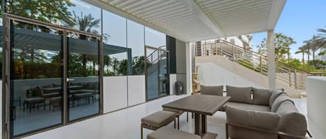 A modern outdoor living space with a glass wall, a wooden table, and a sofa.