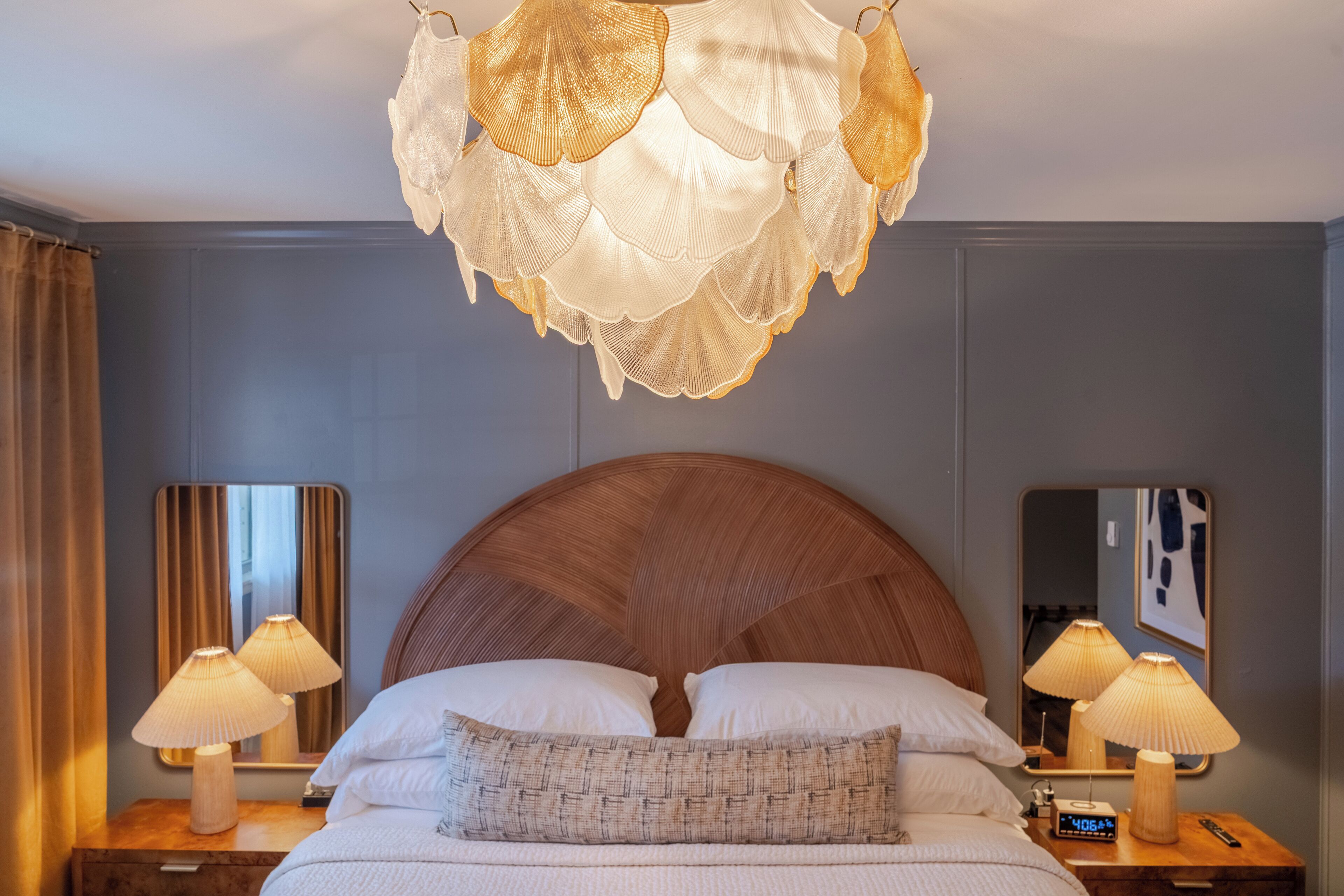 A hotel room with a large bed, two bedside lamps, a mirror, and a chandelier.
