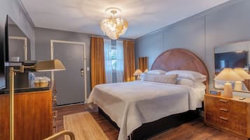 Una habitación de hotel con una cama, lámparas de noche, un espejo, un aparador y piso de madera.