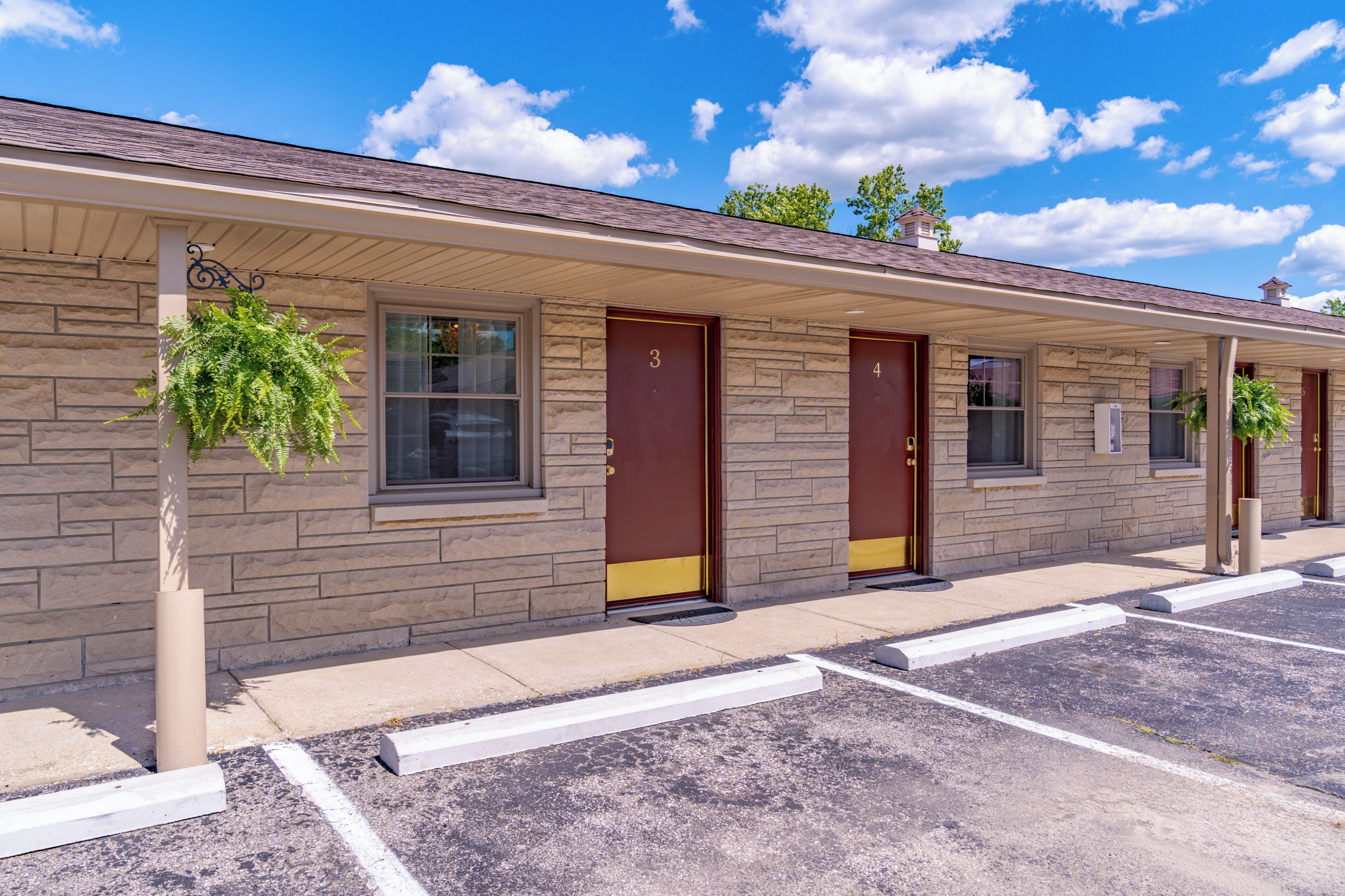 A motel with a row of doors numbered 3 to 4, a parking lot, and a clear sky.
