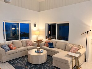 Ein modernes Wohnzimmer mit einem beigefarbenen Ecksofa, einem runden Couchtisch und einem gemusterten Teppich.