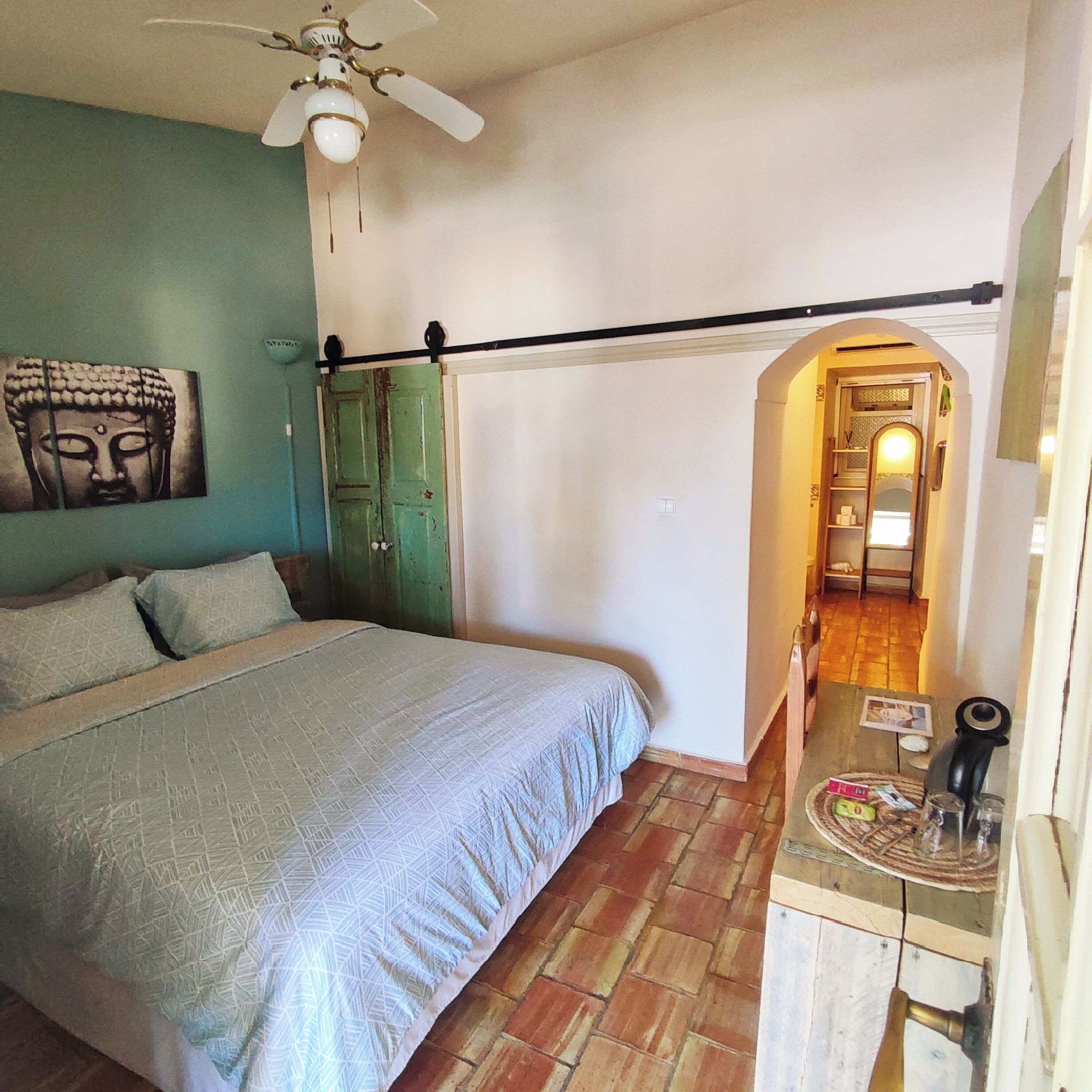 A bedroom with a bed, a ceiling fan, a green door, and a hallway leading to another room.