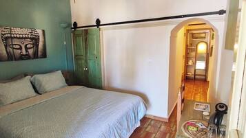 A bedroom with a bed, a ceiling fan, a green door, and a hallway leading to another room.