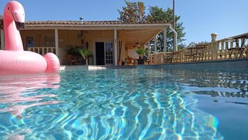 Ein Schwimmbad mit klarem Wasser, einem Flamingo-Schwimmpfau und einem Gebäude mit einem Ziegeldach.