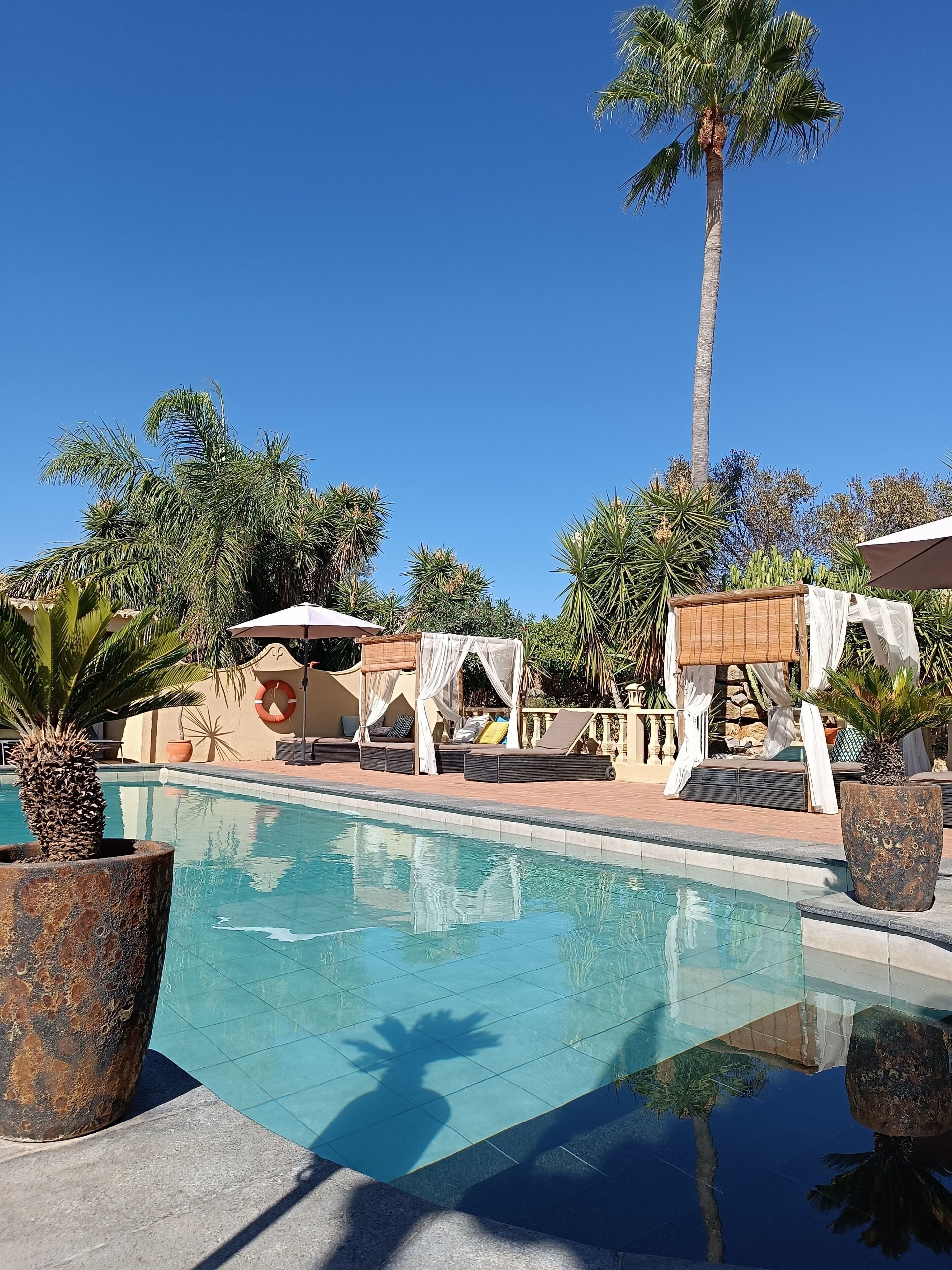Un ciel d’un bleu éclatant, une piscine et des espaces de détente avec des parasols et des coussins.