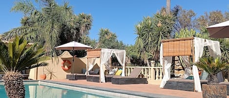 A clear blue sky, a swimming pool, and lounge areas with umbrellas and cushions.