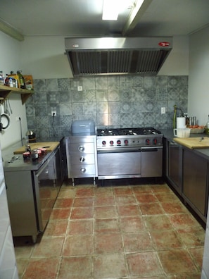 Uma cozinha com fogão a gás, quatro bocas, coifa e painel de azulejos.