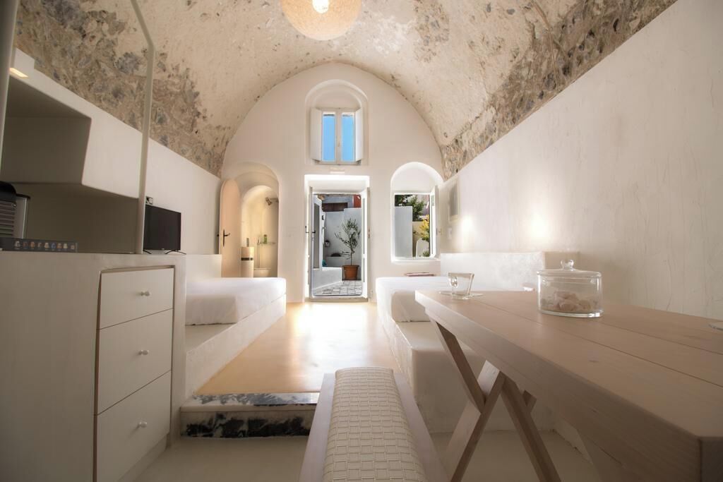A narrow hallway with a white bench, a wooden table, and a glass container on the right.