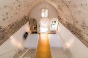 A high-ceilinged room with a central staircase, two beds, a hanging light fixture, and a view through an arched doorway. - Tritiani Traditional House (Messaria)