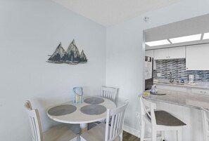 A compact kitchen with white cabinets, a round dining table with chairs, and a wall-mounted artwork of mountains. - Excellent 1-bedroom 1-bath condo with AC in Indian Rocks Beach (Indian Rocks Beach)