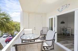 Un balcón con una mesa y sillas de vidrio, una puerta blanca y vistas a un comedor con sillas y una mesa.