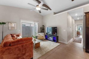 A modern living room with a sofa, coffee table, TV, and a ceiling fan.