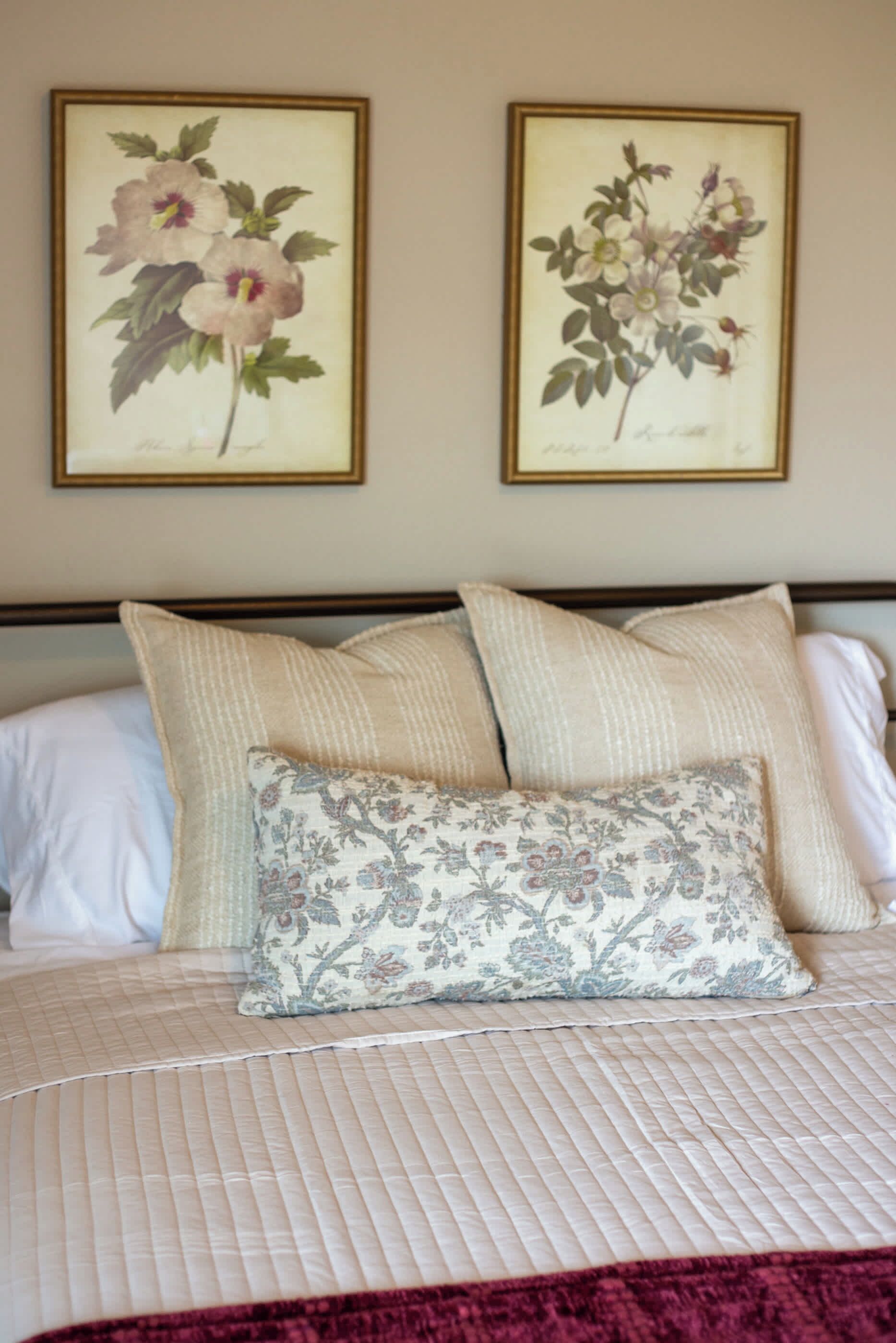 Ein Bett mit gesteppter Bettdecke, zwei Kissen und zwei gerahmte Pflanzenbilder an der Wand.