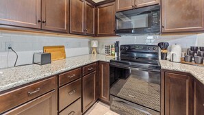 Une cuisine avec des meubles de rangement en bois foncé, un plan de travail en granit, une cuisinière noire et un four à micro-ondes placé au-dessus.