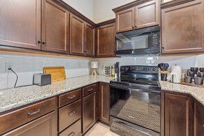 A kitchen with dark wooden cabinets, a granite countertop, a black stove, and a microwave above it. - Beautiful 3 bed 2 bath property with 2 car garage (Wichita)