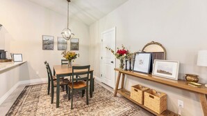 Un coin repas avec une table et des chaises en bois, un lustre, des œuvres d’art encadrées accrochées aux murs et une petite étagère ornée d’objets décoratifs.