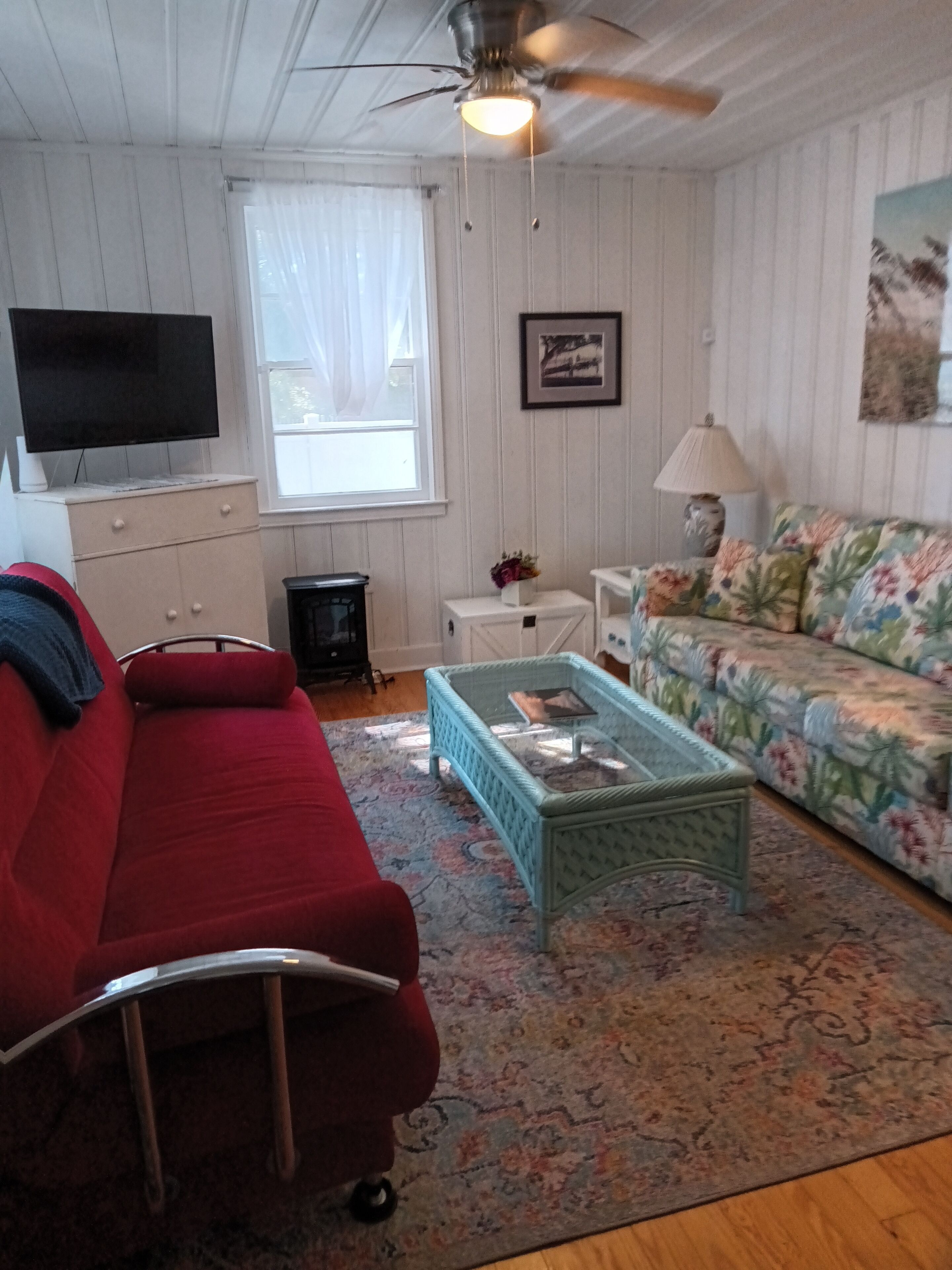 Ein Wohnzimmer mit einem roten Sofa, einem gemusterten Sessel, einem Couchtisch, einem Fernseher und einem Deckenventilator.
