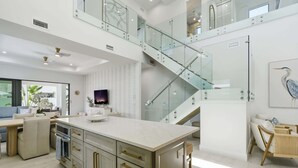 Eine moderne Küche mit einer zentralen Kochinsel, einem Essbereich mit Holztisch und einer Treppe mit Glastrennwand.