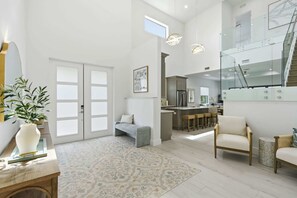 A spacious living area with a large window, a sofa, a coffee table, and a rug. - Brand-New Luxury Pool Home Steps from the Gulf (Naples)