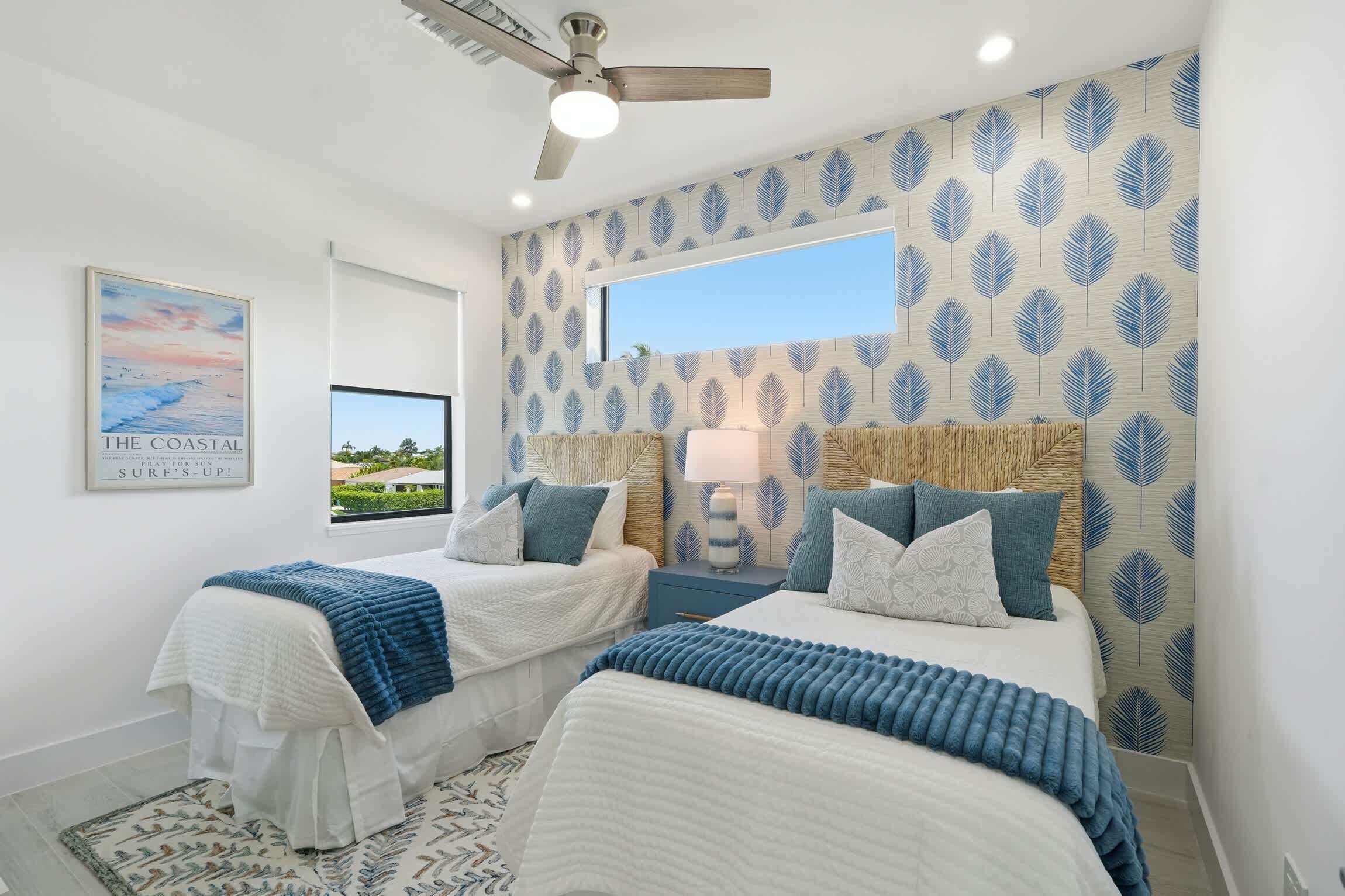 A bedroom with two beds, a ceiling fan, a window, and a beach-themed wall.