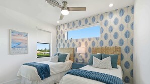Ein Schlafzimmer mit zwei Betten, einem Deckenventilator, einem Fenster und einer Wand im Strandhausstil.