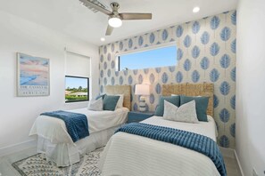 Ein Schlafzimmer mit zwei Betten, einem Deckenventilator, einem Fenster und einer Wand im Strandhausstil.