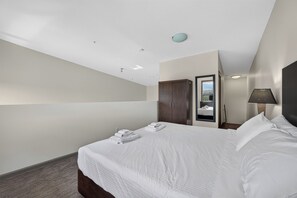 A hotel room with a large bed, a wardrobe, a mirror, and a view of the city. - 2 Bd Loft 603 at Playa. Pool and Hot Tub (Kelowna)