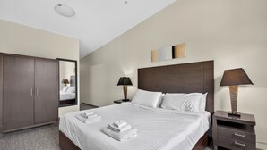 Una habitación de hotel con una cama grande, un armario, una mesita de noche y una mesita auxiliar.