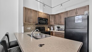 Una cocina moderna con armarios de madera, un lavamanos de acero inoxidable, un refrigerador negro y un microondas.