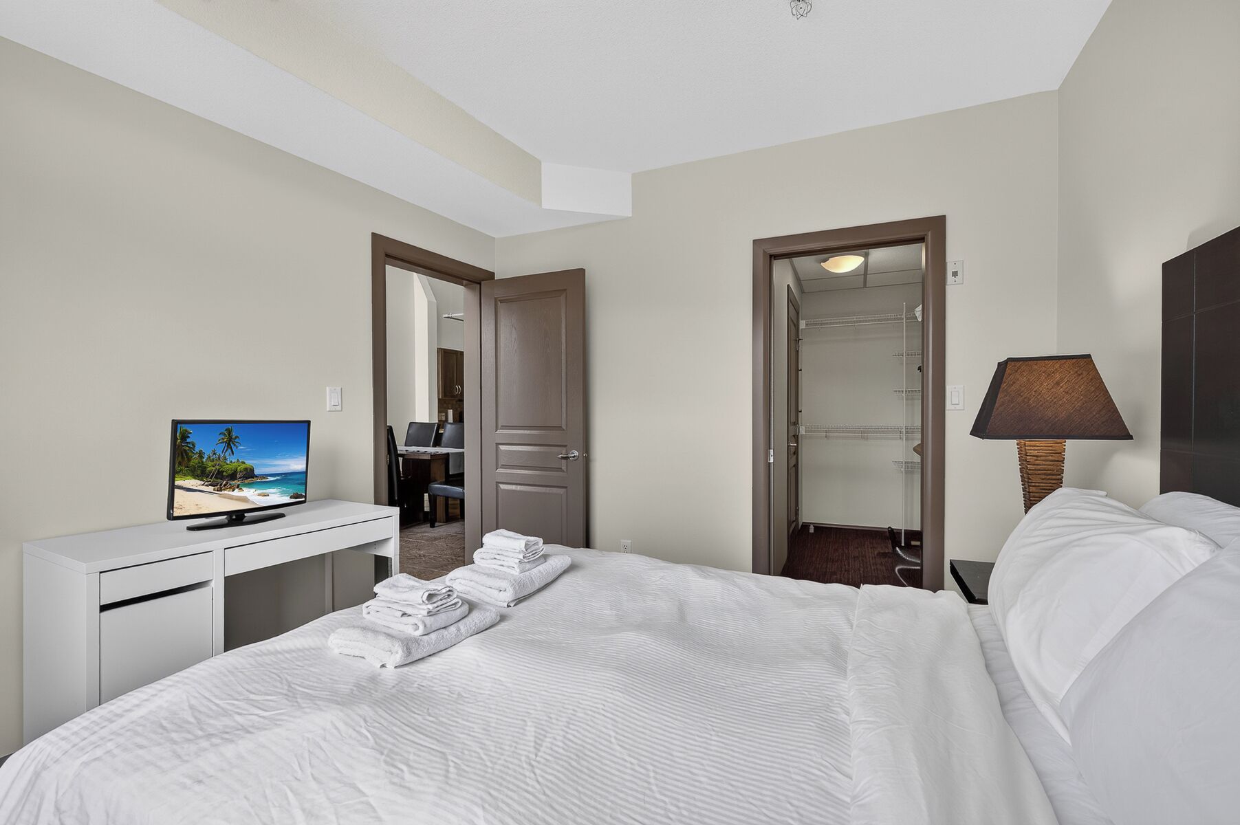Een hotelkamer met een bed, een bureau met een televisie, een lamp en een badkamer door een geopende deur zichtbaar.