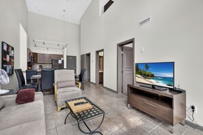 A modern living room with a flat-screen TV, a sofa, a coffee table, and a kitchen area in the background. - 2 Bd Loft 603 at Playa. Pool and Hot Tub (Kelowna)