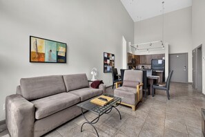 A modern living room with a grey sofa, a glass coffee table, and a dining area with a chair and a table. - 2 Bd Loft 603 at Playa. Pool and Hot Tub (Kelowna)