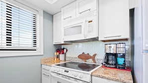 A compact kitchen with white cabinets, a microwave, a stove, and a coffee maker. - Santa Rosa Dunes 321 (Pensacola Beach)