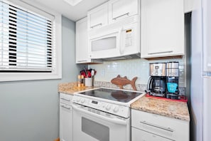 A compact kitchen with white cabinets, a microwave, a stove, and a coffee maker. - Santa Rosa Dunes 321 (Pensacola Beach)