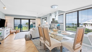 A modern living room with a dining area, large windows, and a view of the outdoors. - Santa Rosa Dunes 321 (Pensacola Beach)