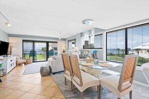 A modern living room with a dining area, large windows, and a view of the outdoors. - Santa Rosa Dunes 321 (Pensacola Beach)