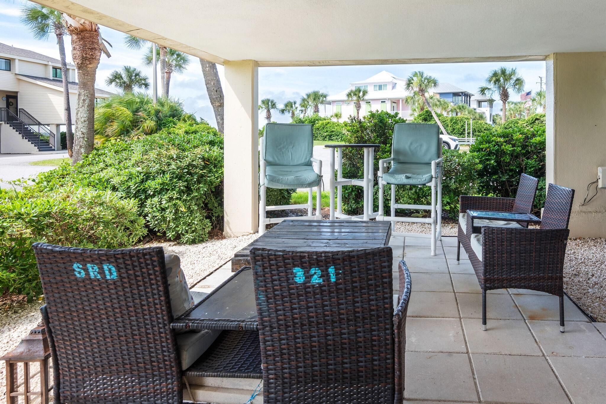 An outdoor patio with wicker furniture, including chairs and a table, and a view of a residential area with houses and palm trees.